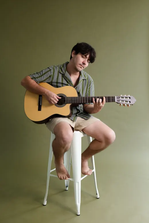 Leonel tocando violão sentado, em estúdio